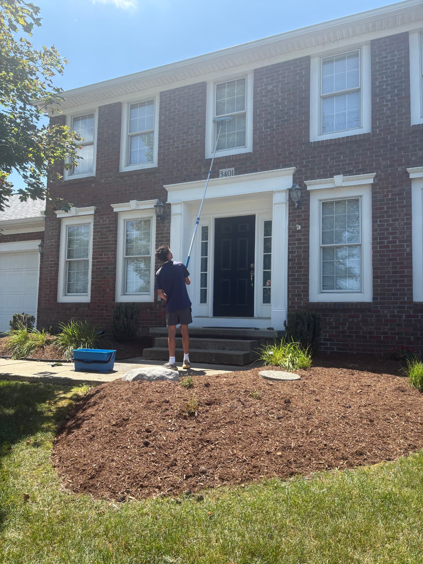 Technician cleaning second-story windows on a brick colonial home